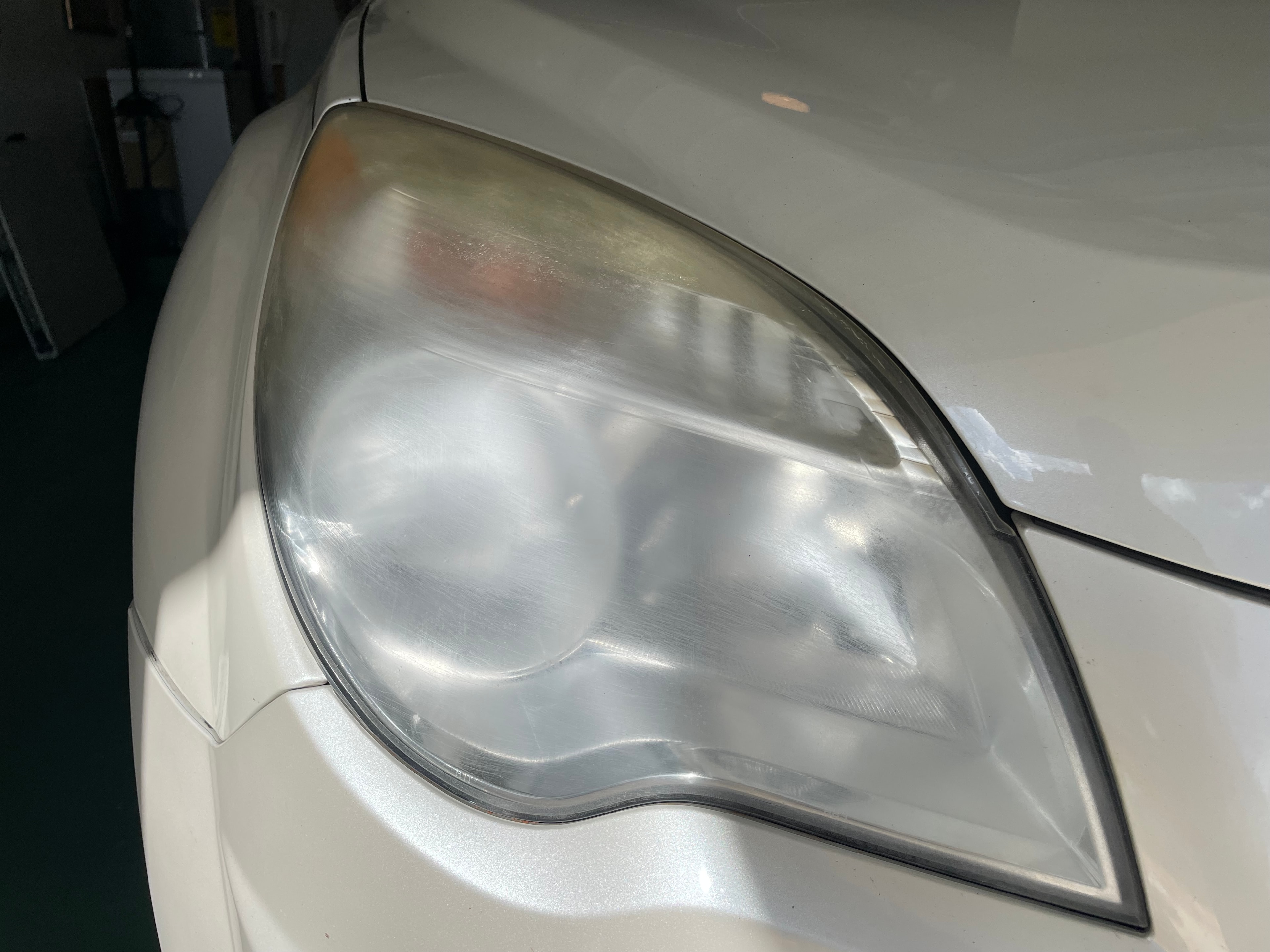 Foggy oxidized headlight before restoration on white vehicle